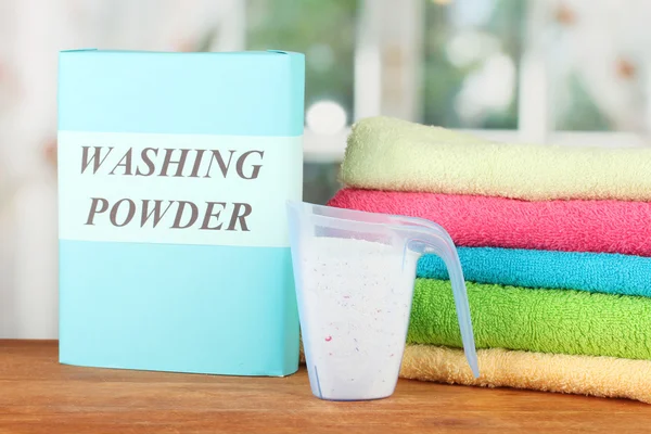 Box of washing powder with blue measuring cup and towels, on wooden table c — Stock Photo, Image