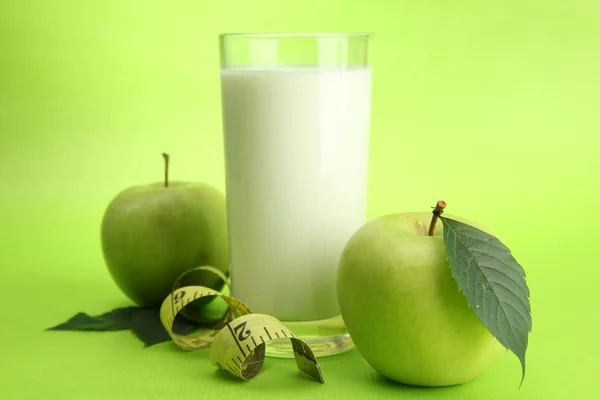 Glass of kefir, apples and measuring tape, on green background — Stock Photo, Image