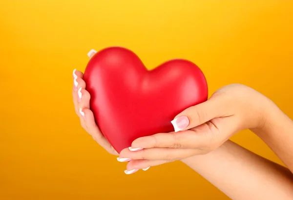 Rood hart in handen van de vrouw, op oranje achtergrond close-up — Stockfoto