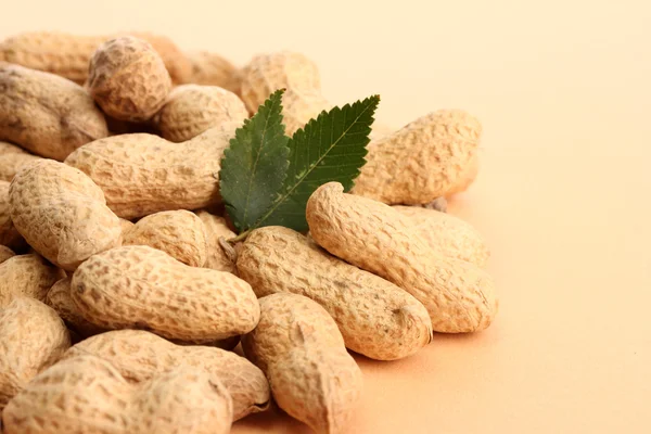 Вкусный арахис с зелеными листьями, на бежевом фоне — стоковое фото