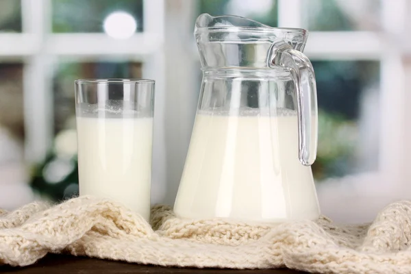 Pichet et verre de lait sur col rond tricot sur table en bois sur fenêtre b — Photo