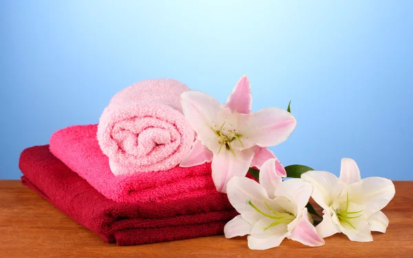 Stack of towels with pink lily on blue background — Stock Photo, Image