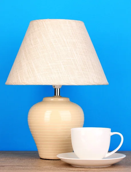 Table lamp and cup on blue background — Stock Photo, Image