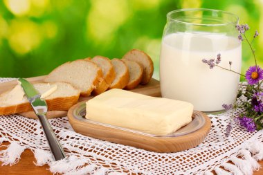 Doğal arka planda ekmek ve sütle çevrili ahşap tutacağa tereyağı.