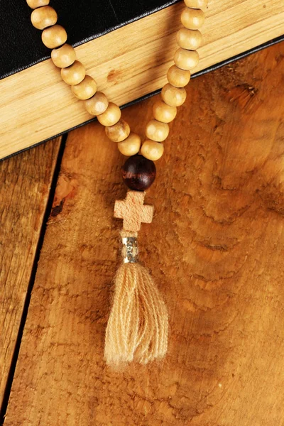 O rosário de madeira contas e bíblia sagrada no fundo de madeira close-up — Fotografia de Stock