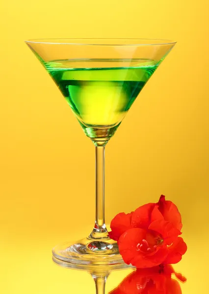 Glass with cocktail and gladiolus bud on yellow background close-up — Stock Photo, Image