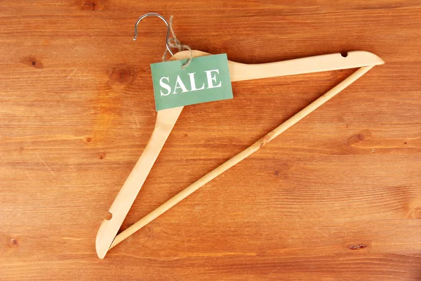 Coat hanger with sale tag on wooden background — Stock Photo, Image