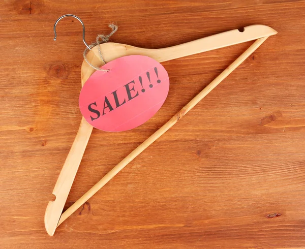 Coat hanger with sale tag on wooden background — Stock Photo, Image