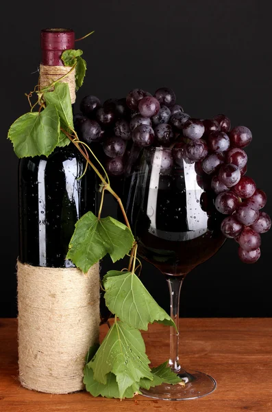 Bottle of wine with grape leaves on wooden table on black background — Stock Photo, Image