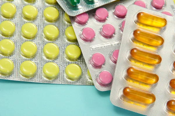 Капсули та таблетки, упаковані в пухирі, на синьому фоні — стокове фото