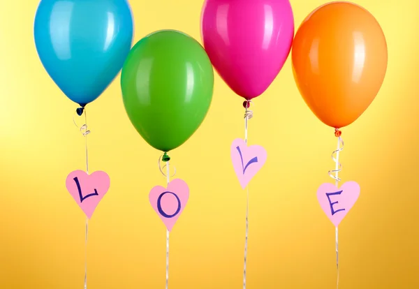 Kleurrijke ballonnen houdt woord liefde op gele achtergrond — Stockfoto