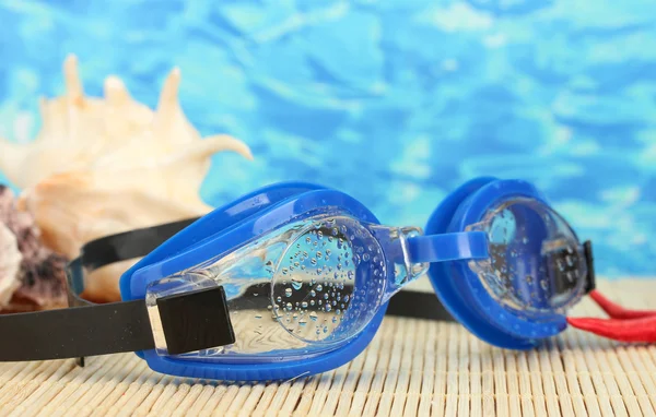 Blauwe zwemmen bril met druppels op een bamboe pad, op blauwe zee achtergrond — Stockfoto