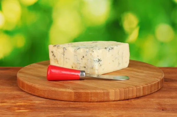 Cheese with mold and knife on the cutting board on bright green background — Stock Photo, Image