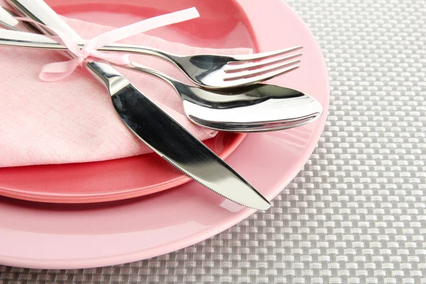 Розовые пустые тарелки с вилкой, ложкой и ножом на серой скатерти — стоковое фото
