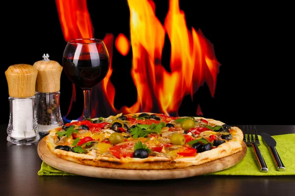 Deliciosa pizza con copa de vino tinto y especias en mesa de madera en el fuego b — Foto de Stock