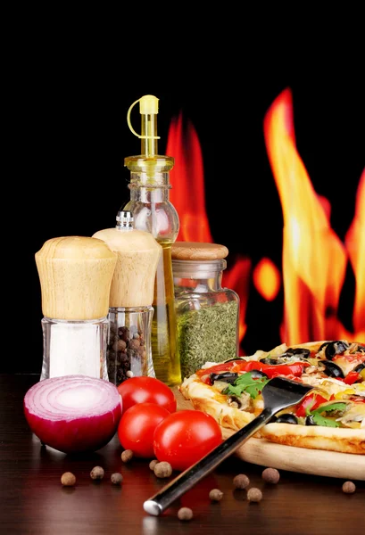 Delicious pizza with spices on wooden table on fire background — Stock Photo, Image