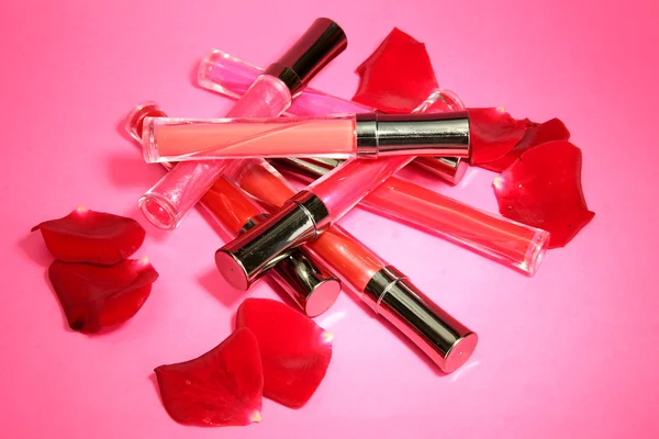 Mooie lip glossen met rozenblaadjes, op roze achtergrond — Stockfoto