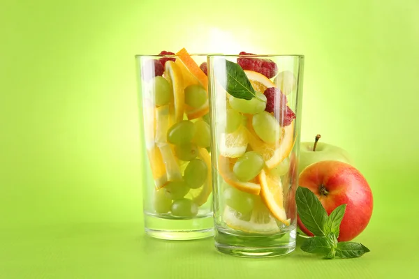 Transparent glasses with citrus fruits, on grren background — Stock Photo, Image