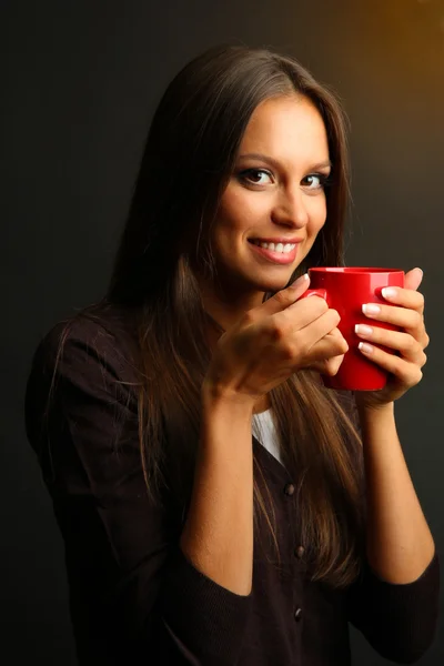 Mooie jonge vrouw met een kopje koffie, op bruine achtergrond — Stockfoto