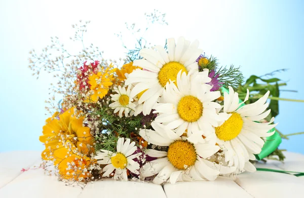 Beautiful bouquet of bright wildflowers, on wooden table on blue backgroun — Stock Photo, Image