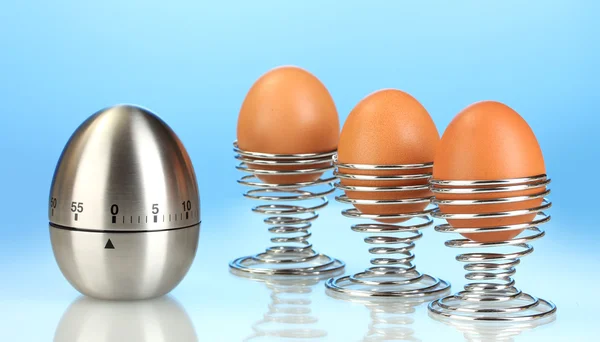 egg timer and egg in metal stand on blue background