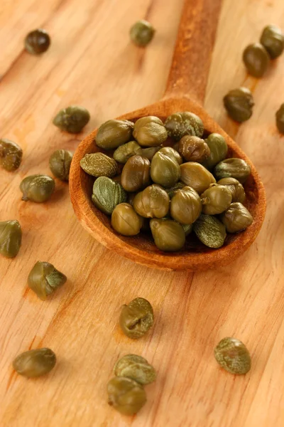 Green capers in wooden spoon on wooden background close-up — Stock Photo, Image