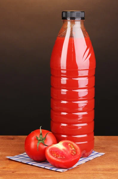 Tomato juice in bottle on wooden table on brown background — Stock Photo, Image