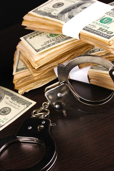 Handcuffs and packs of dollars on wooden table close-up — Stock Photo, Image