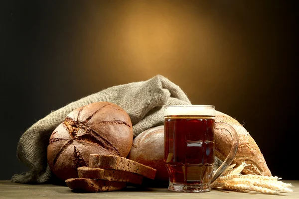 Tankard de kvass y panes de centeno con orejas, sobre mesa de madera sobre fondo marrón —  Fotos de Stock