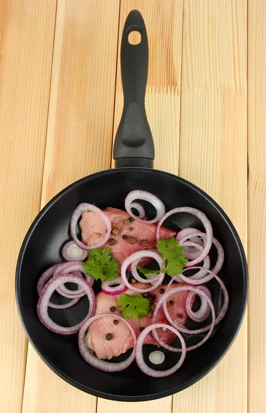 A pieces of pork with onions fried in pan on wooden table