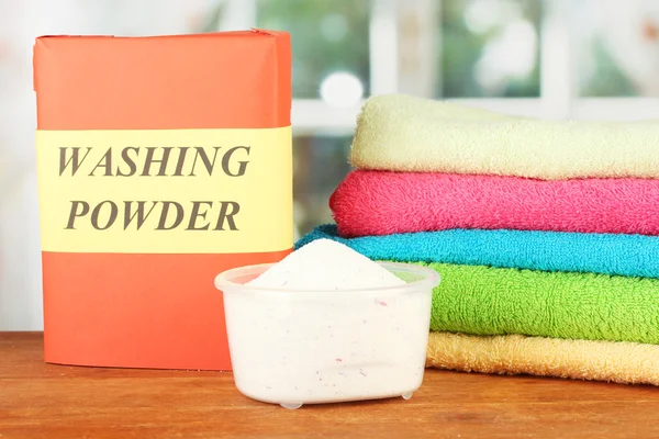 Box of washing powder with blue measuring cup and towels, on wooden table c — Stock Photo, Image