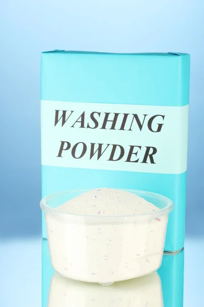Box of washing powder with measuring cup, on blue background close-up — Stock Photo, Image