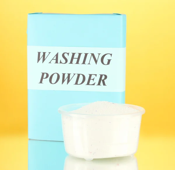 Box of washing powder with measuring cup, on orange background close-up — Stock Photo, Image