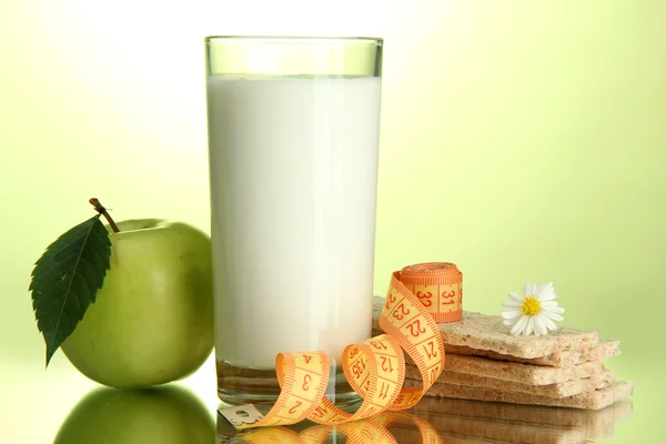 Glas van kefir, apple, crispbreads en meetlint, op groene achtergrond — Stockfoto