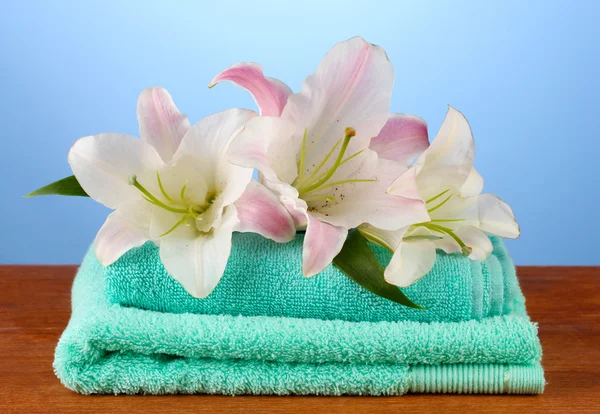 Stack of towels with pink lily on blue background — Stock Photo, Image