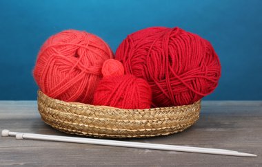 mavi zemin üzerine ahşap masa üzerinde sepet içinde kırmızı örgüler iplikler