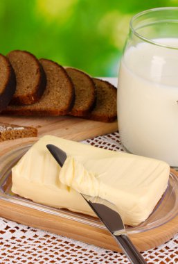 Doğal arka planda ekmek ve sütle çevrili ahşap tutacağa tereyağı.