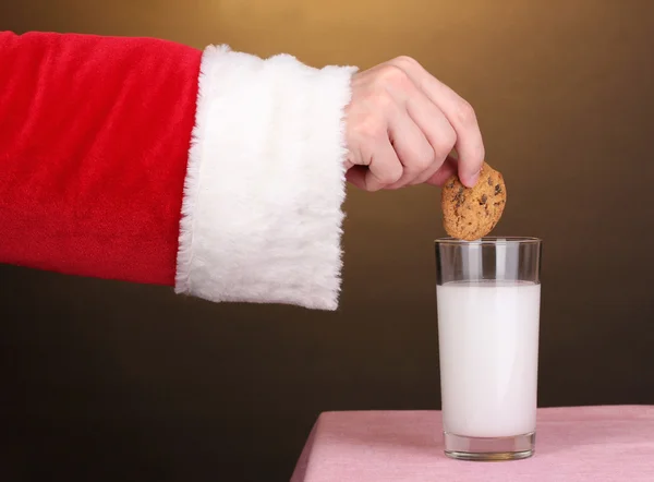 Santa claus ruka drží čokolády cookie na hnědé pozadí — Stock fotografie