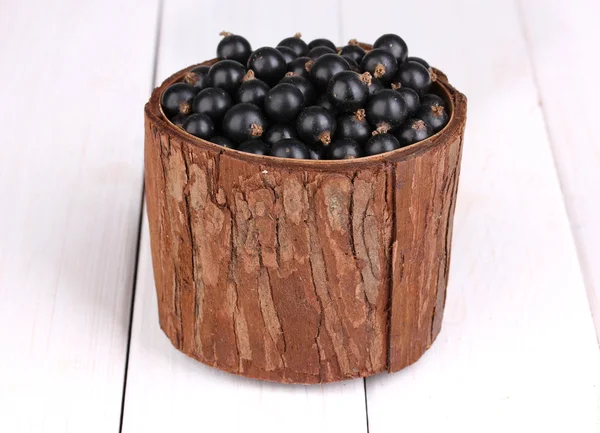 Black currant in wooden cup on wooden background — Stock Photo, Image