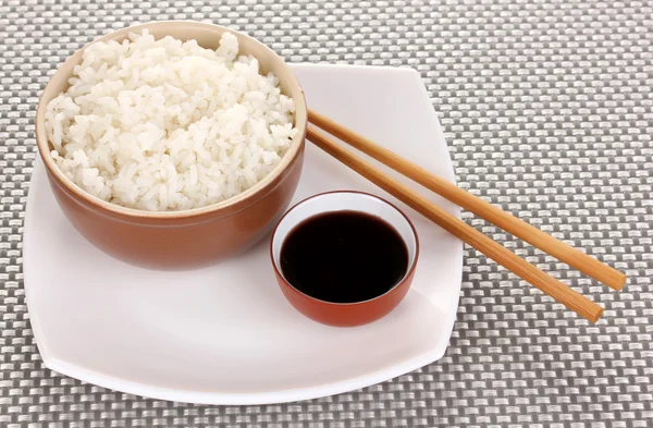 Tigela de arroz e pauzinhos no prato no tapete cinza — Fotografia de Stock