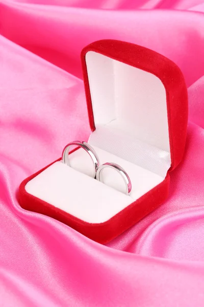 Anillos de boda en caja roja sobre fondo de tela rosa —  Fotos de Stock