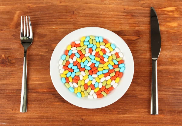 A lot of pills in a plate with knife and fork on wooden background close-up — Stock Photo, Image