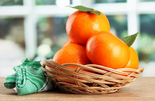 Tangerines with leaves in a beautiful basket, on wooden table on window bac — Stock Photo, Image