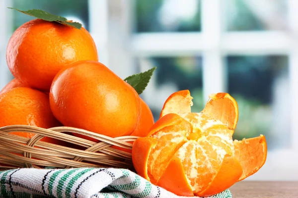 Tangerines with leaves in a beautiful basket, on wooden table on window bac — Stock Photo, Image