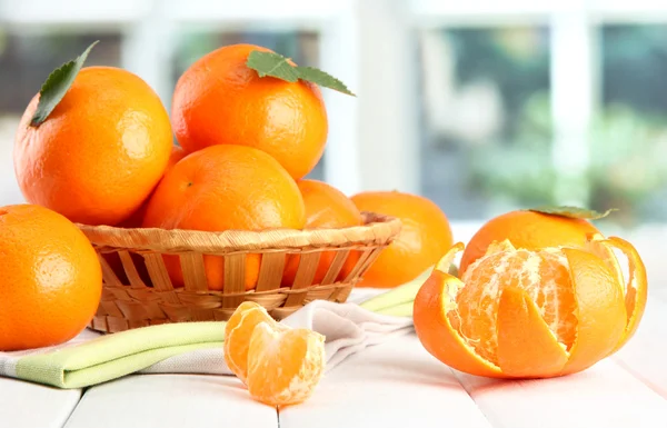 Tangerines with leaves in a beautiful basket, on wooden table on window bac — Stock Photo, Image