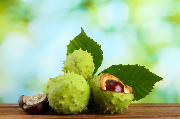 Castagne con foglie su tavolo di legno su sfondo verde — Foto Stock