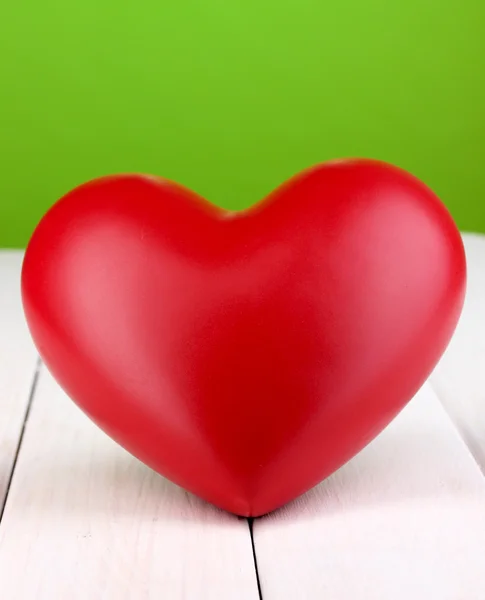 Coração vermelho decorativo na mesa de madeira branca no fundo verde — Fotografia de Stock