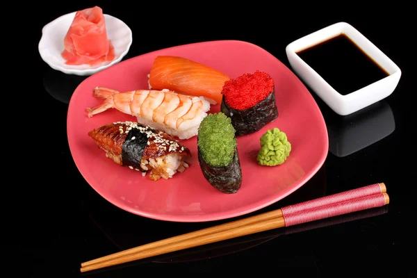 Heerlijke sushi geserveerd op rode plaat geïsoleerd op zwart — Stockfoto