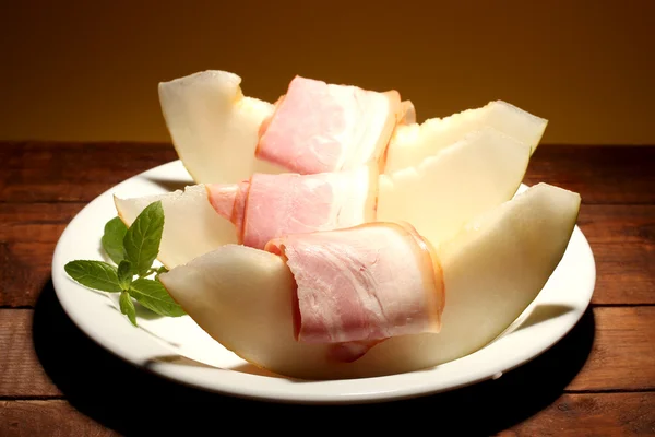 Parma ham and melon, on wooden table, on yellow background — Stock Photo, Image