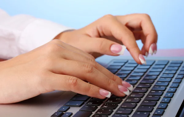 Mani della donna d'affari digitando sul computer portatile, su sfondo blu chiudere - — Foto Stock